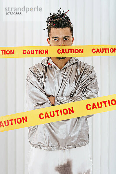 Young man standing behind restriction tapes with mouth covered in front of wall