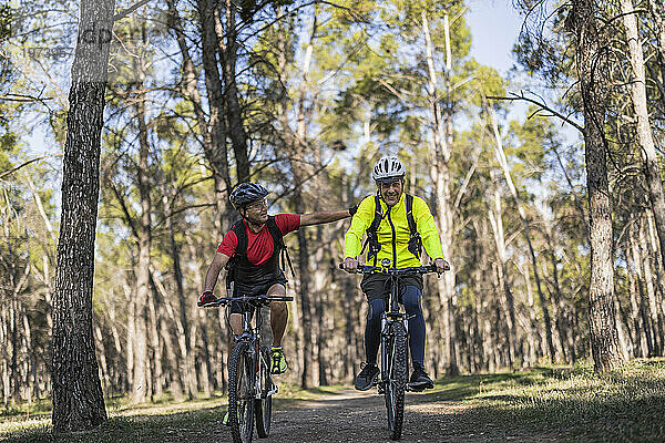 Glücklicher Mann unterstützt Freund und fährt Fahrrad im Wald