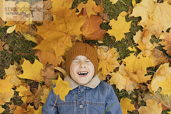 Fröhlicher Junge liegt auf fallenden gelben Herbstblättern im Park