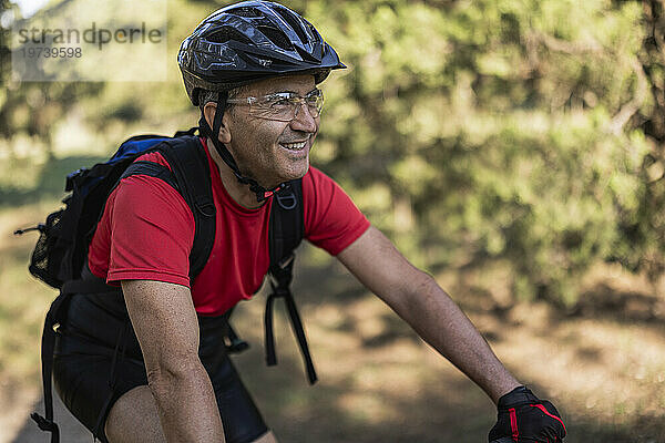 Lächelnder Mann mit Helm und Radfahren im Wald