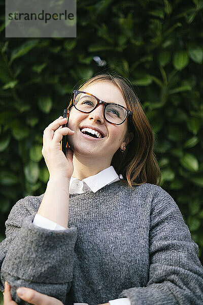 Glückliche junge Frau mit Brille  die auf dem Handy spricht