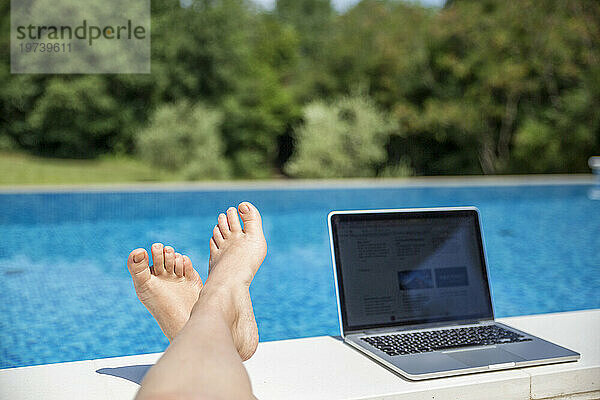 Fuß einer Frau in der Nähe eines Laptops am Pool an einem sonnigen Tag