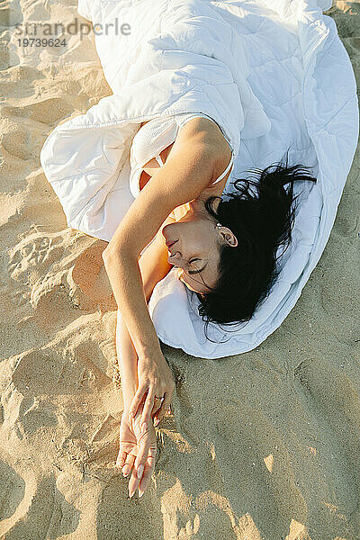 Frau mit geschlossenen Augen  in eine Decke gehüllt  liegt am Strand