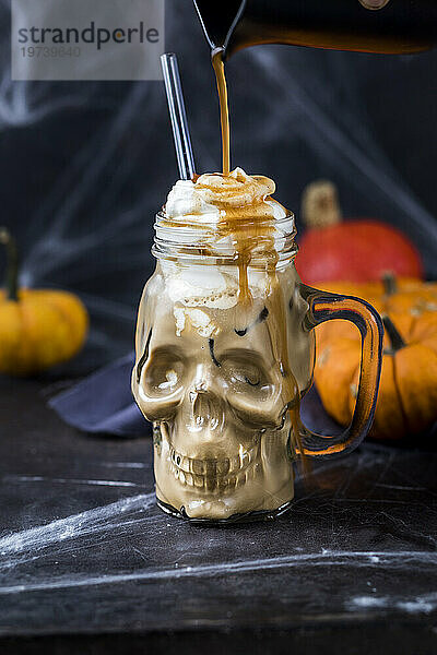 Syrup pouring on skull shaped mug of pumpkin spice latte with whipped cream