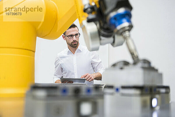 Ingenieur mit Tablet-PC bedient Roboterarm in der Fabrik