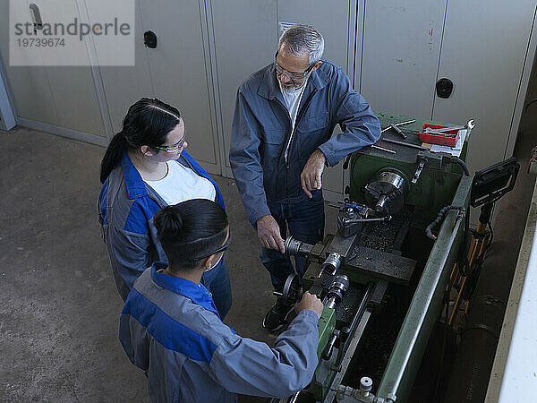 Instructor discussing with apprentices standing near lathe machine at workshop