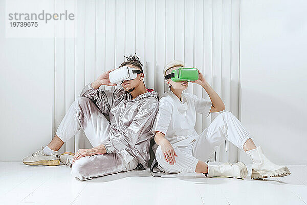 Man and woman using virtual reality headset sitting back to back in front of wall