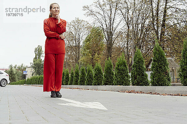 Frau mit Hand am Kinn steht neben Pfeilschild an der Straße