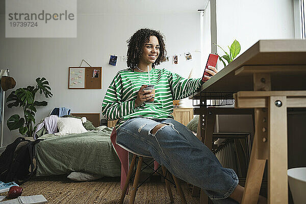 Happy teenage girl using smart phone at desk in bedroom