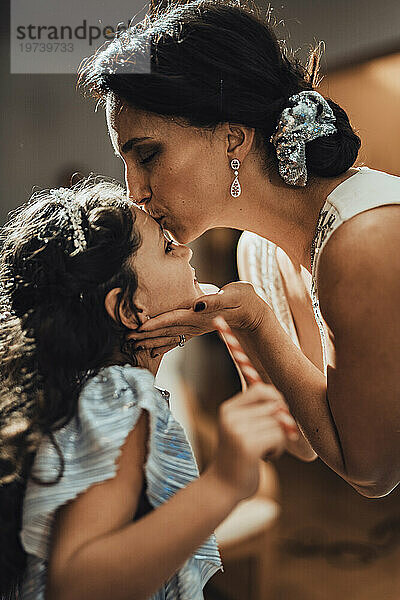 Mother kissing daughter on forehead at home