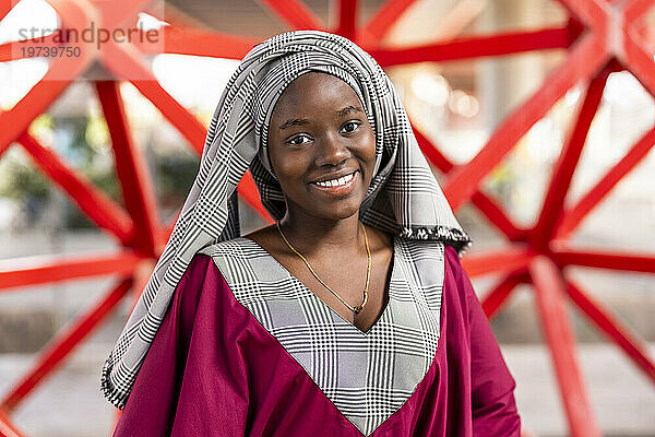 Lächelnde junge Frau mit Hijab steht vor dem Geländer
