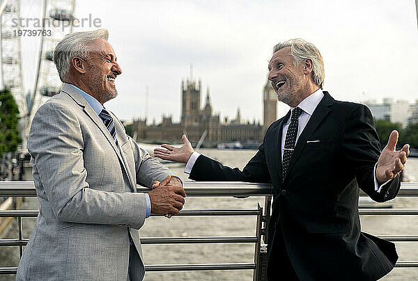 Fröhliche ältere Geschäftsleute reden auf der Brücke in der Nähe des Geländers miteinander
