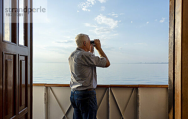 Mann schaut vom Schiff aus durch ein Fernglas aufs Meer