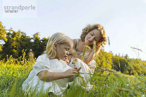 Lächelnde Mutter und Tochter kauern im Gras