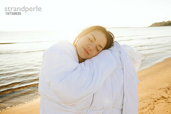 Happy woman with eyes closed leaning head on blanket at beach