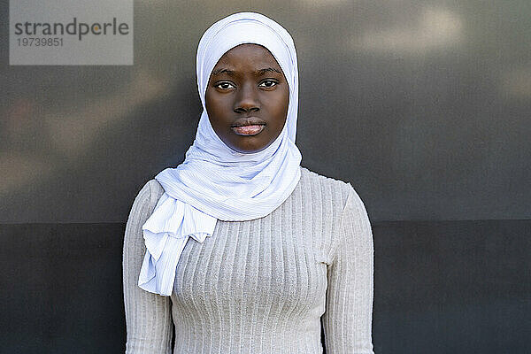 Junge Frau mit Hijab steht vor grauer und schwarzer Wand