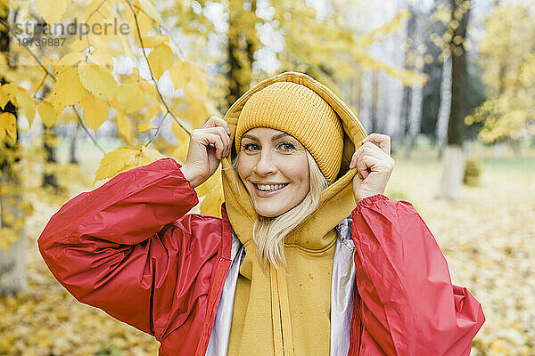 Lächelnde Frau mit Regenmantel und Strickmütze im Park