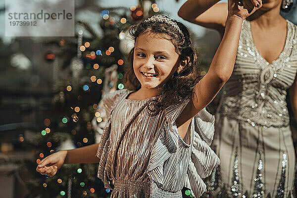 Lächelnde Tochter hält Mutters Hand und tanzt zu Hause neben dem Weihnachtsbaum