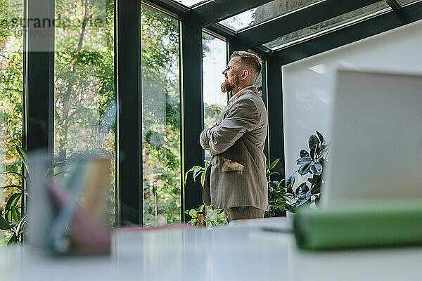 Nachdenklicher Geschäftsmann blickt durch Fenster im Büro