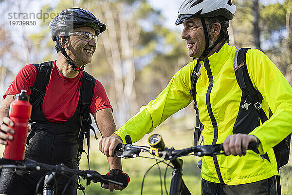 Glücklicher Mann steht mit Freund neben Fahrrad und hält Wasserflasche im Wald