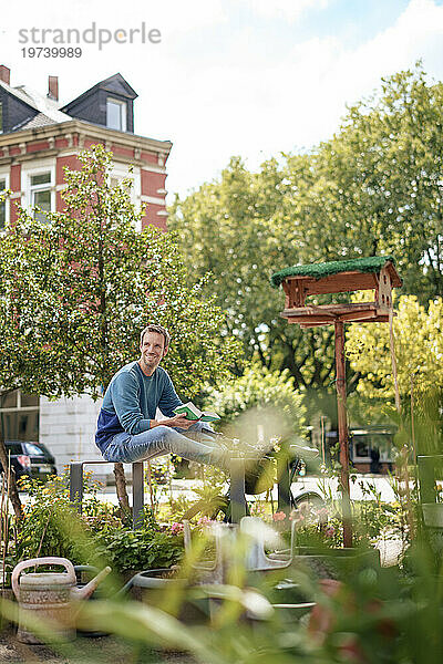 Smiling man holding book sitting in garden