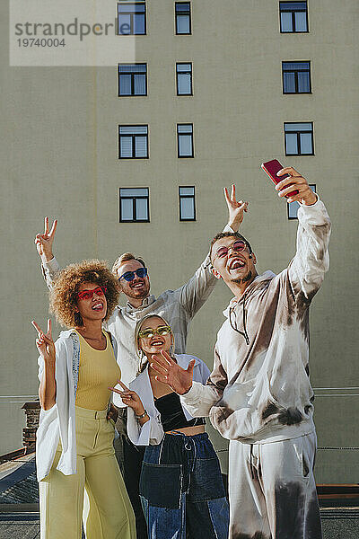 Lächelnder Mann macht Selfie mit Freunden per Smartphone auf dem Dach