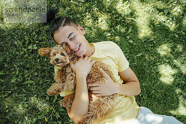 Smiling man holding dog and lying on grass in park