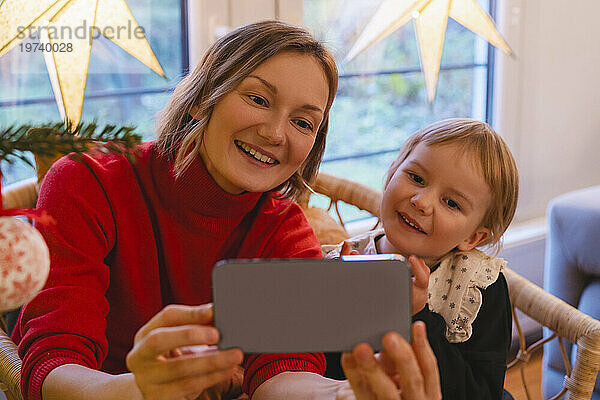 Lächelnde Mutter und Tochter schauen zu Hause auf das Handy