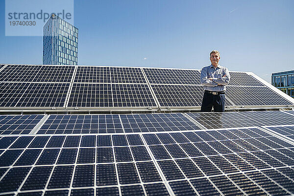 Ein selbstbewusster männlicher Unternehmer  der stolz inmitten eines Feldes aus Solarpaneelen steht