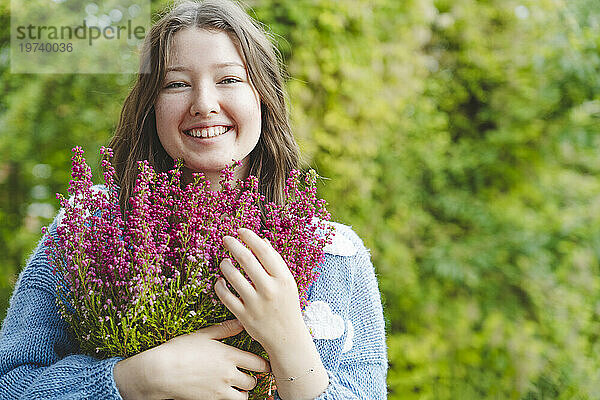 Lächelndes Mädchen hält Heideblüten vor Pflanzen