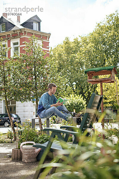 Smiling man reading book sitting in front of trees