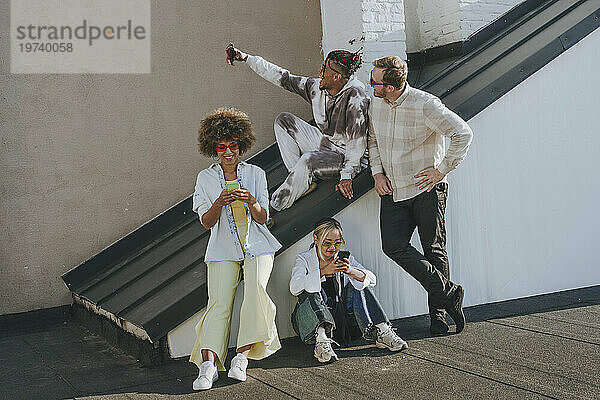 Happy friends taking selfie and using smart phones on rooftop
