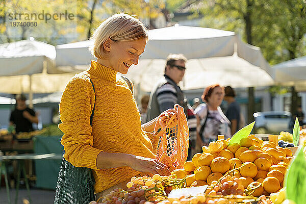 Lächelnde Frau kauft Mandarinen auf dem Bauernmarkt