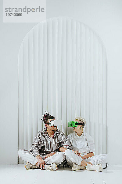 Freunde tragen Virtual-Reality-Headset und sitzen auf dem Boden vor der Wand
