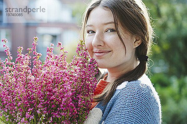 Smiling girl holding heather flowers on sunny day