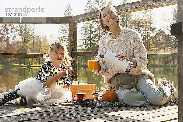 Glückliches Mädchen mit Mutter  die auf der Fußgängerbrücke heiße Schokolade in eine Tasse gießt