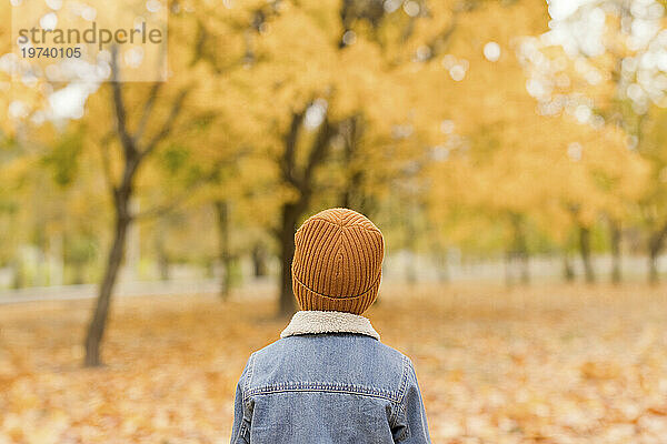 Junge trägt Jeansjacke und gelbe Strickmütze im Herbstpark