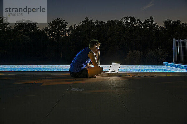 Freiberufler arbeitet nachts am Laptop in der Nähe des Schwimmbades