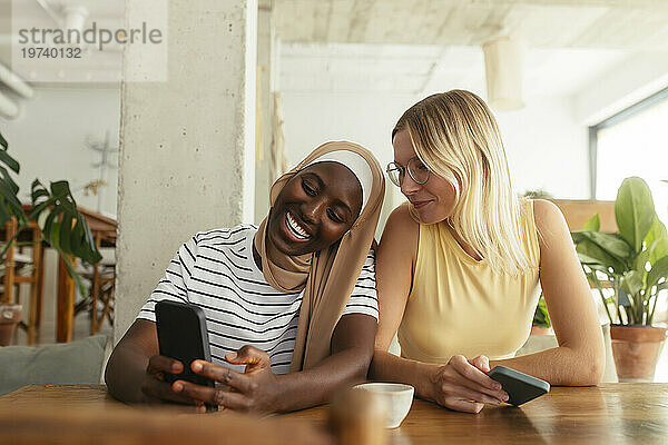 Smiling woman showing smart phone to friend at coffee shop