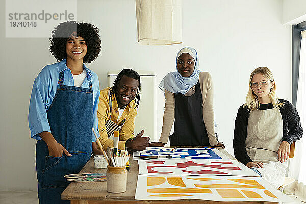 Lächelnde Künstler am Schreibtisch mit Gemälden im Atelier