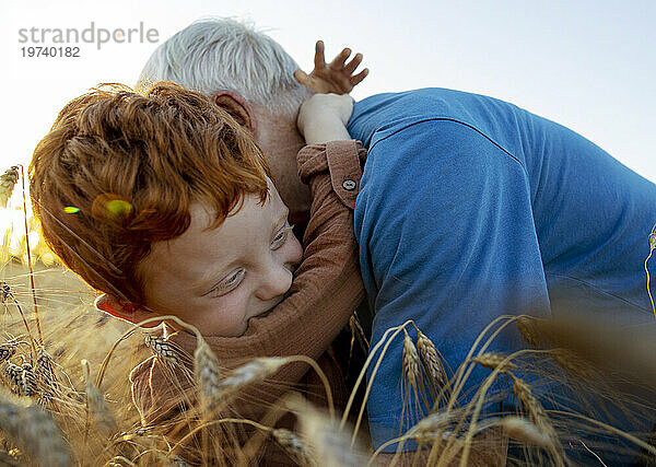 Lächelnder Enkel umarmt Großvater im Weizenfeld