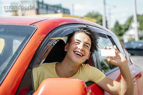 Smiling man showing driver's license and leaning out of car window