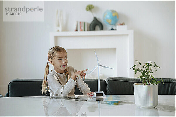 Mädchen berührt Windturbinenmodell auf Tisch im Wohnzimmer zu Hause