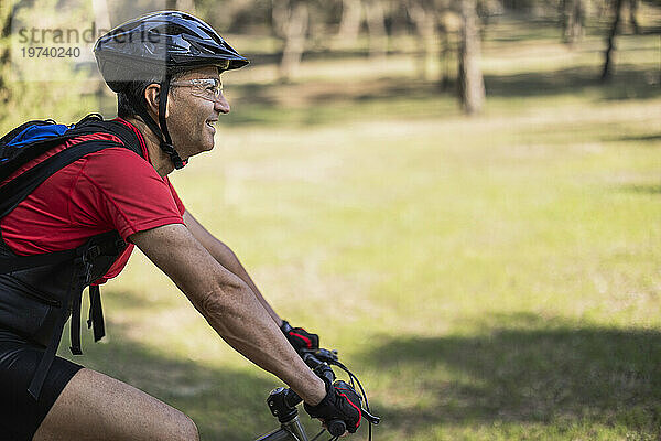 Glücklicher Mann mit Helm und Radfahren im Wald an einem sonnigen Tag