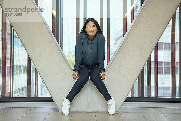 Lächelnde Geschäftsfrau sitzt auf einer architektonischen Säule im Büro