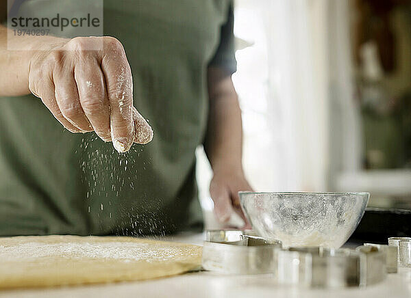 Senior woman sprinkling flour on dough at home