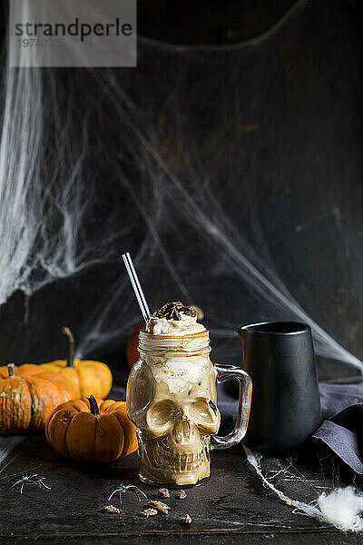 Skull shaped mug of pumpkin spice latte with whipped cream and caramelized pumpkin seeds