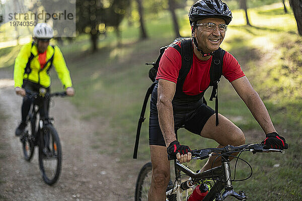 Lächelnder Mann fährt Fahrrad mit Freund im Wald