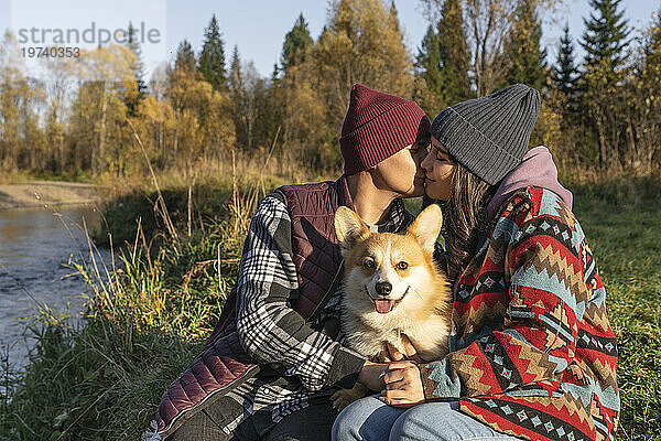 Mann küsst Frau mit Hund am Wochenende im öffentlichen Park