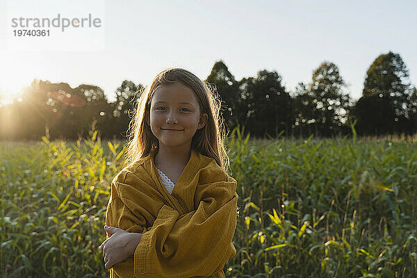 Smiling girl standing with arms crossed in field